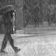 Photo en noir et blanc d'un homme marchant sous la pluie dans une rue
