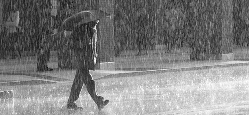 Photo en noir et blanc d'un homme marchant sous la pluie dans une rue